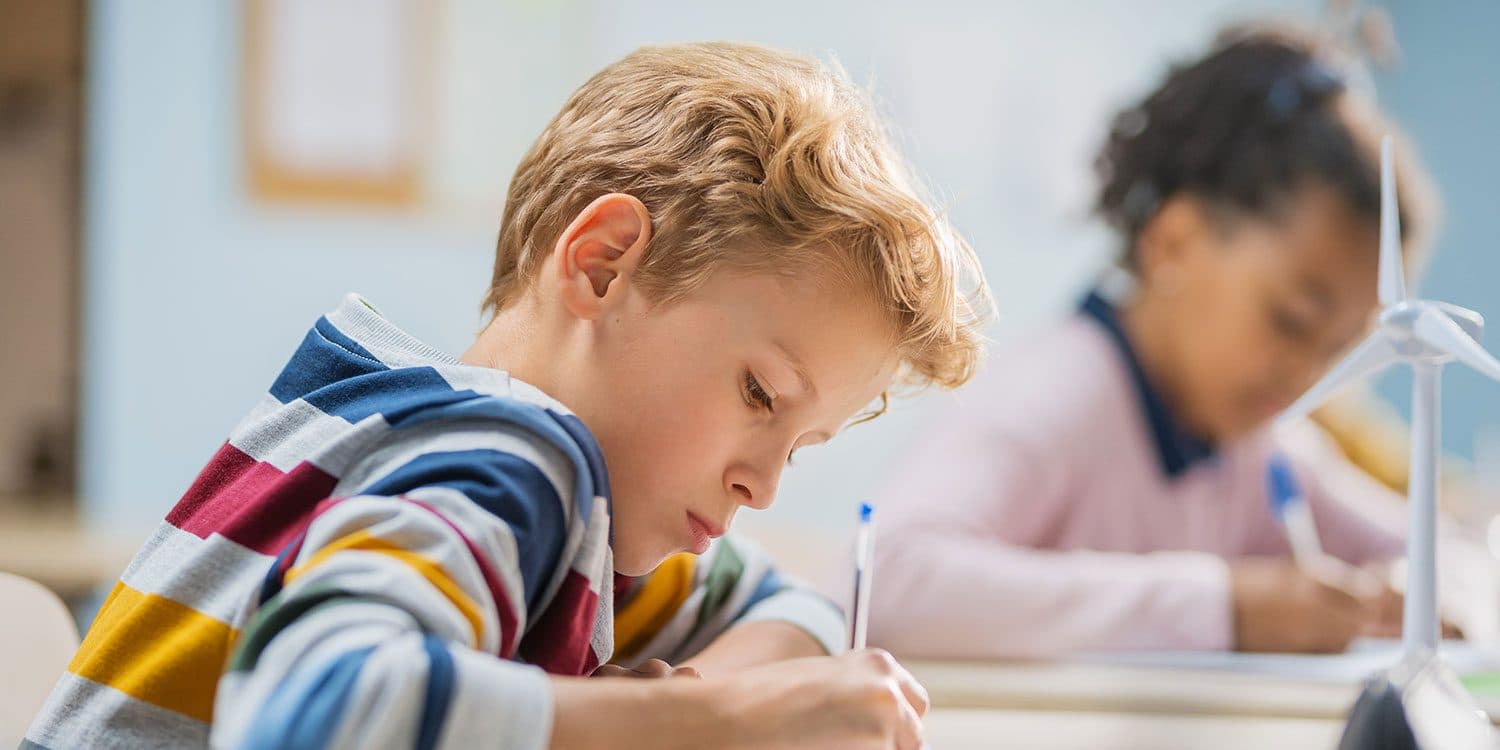 Student writing at a classroom desk.