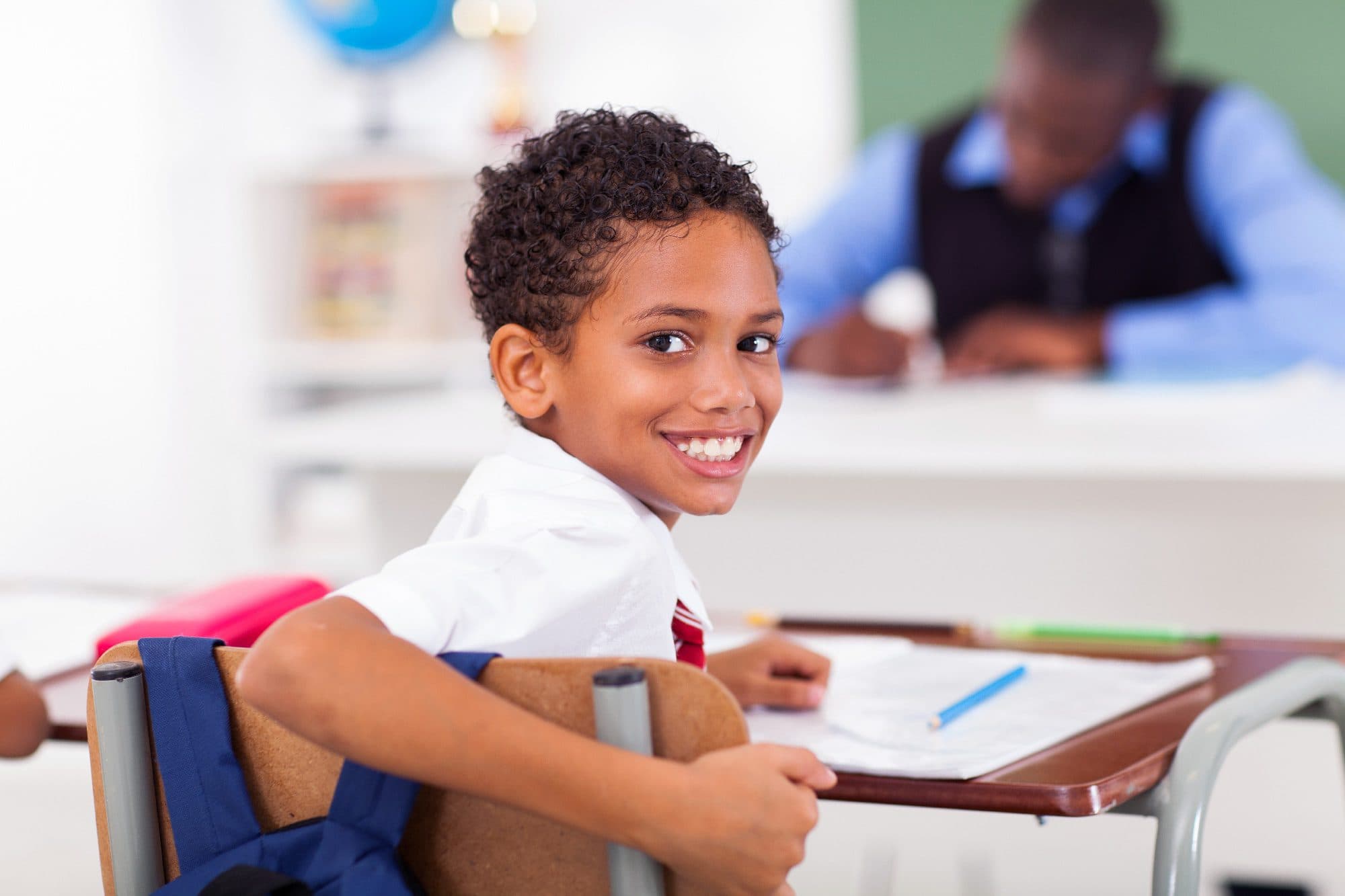 Smiling student turning around at a classroom desk.