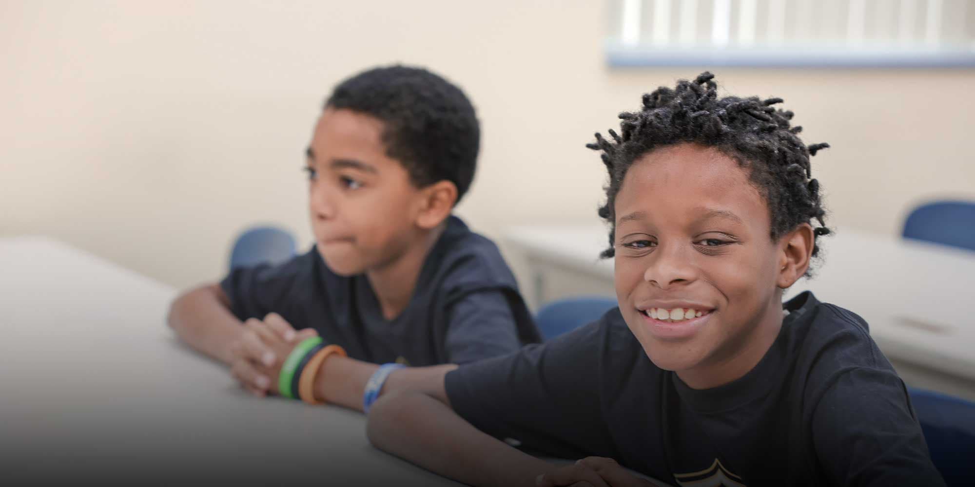 Two students seated at a classroom table, one smiling at the camera.